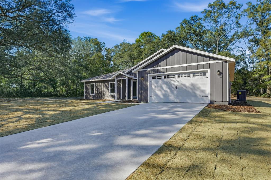A single-story house with gray vertical siding, a white garage door, and a concrete driveway — TBD SW 170TH STREET, ARCHER, FL