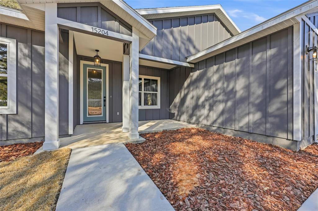 The exterior view shows a gray house with a covered entryway and a blue door — TBD SW 170TH STREET, ARCHER, FL