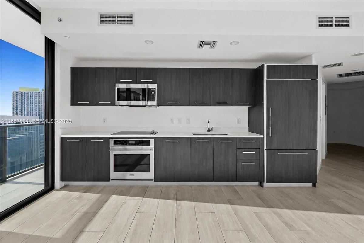 A modern kitchen features dark wood cabinetry, stainless steel appliances, and light wood flooring — 55 SW 9th ST # 3006, Miami FL 33130, MIAMI, FL