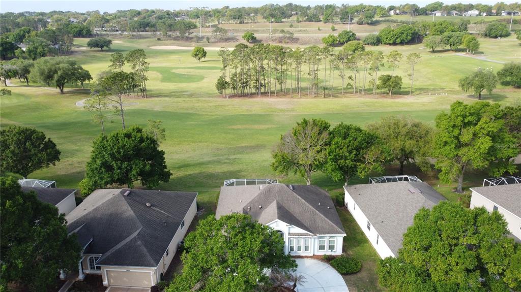 An aerial view shows three suburban houses bordering a large, open golf course — 3828 AVON COURT, CLERMONT, FL