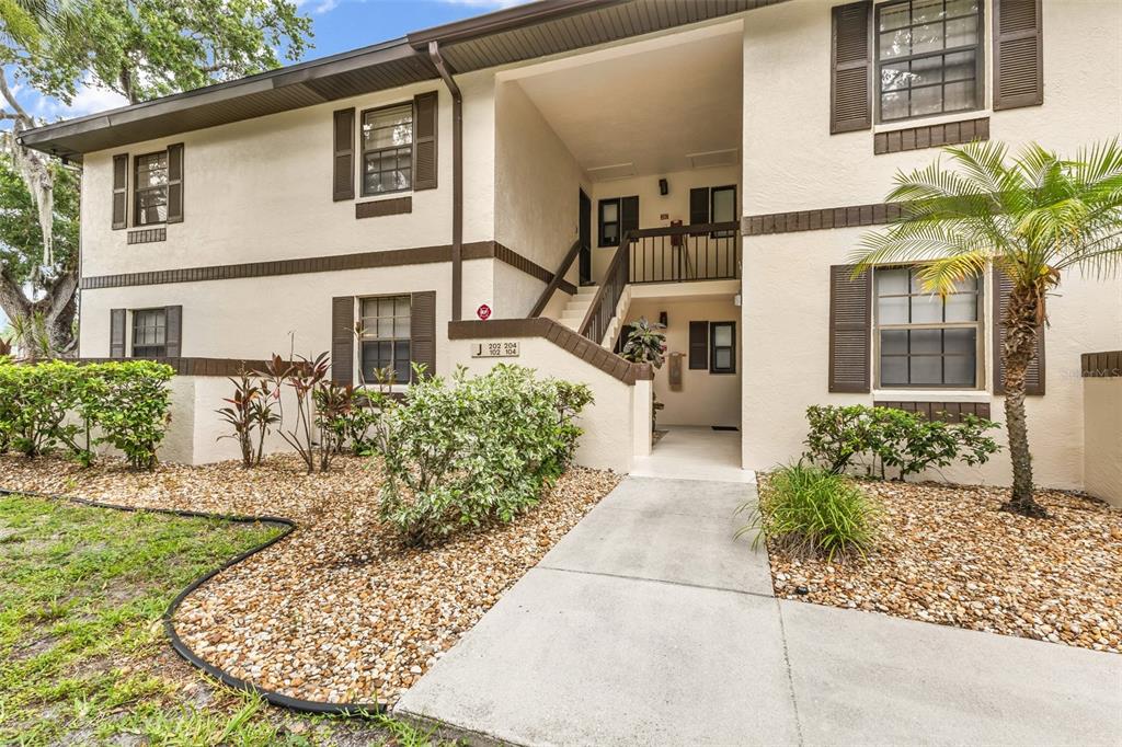 A two-story apartment building exterior with a central staircase and a landscaped front yard — 19505 QUESADA AVENUE UNIT J204, PORT CHARLOTTE, FL