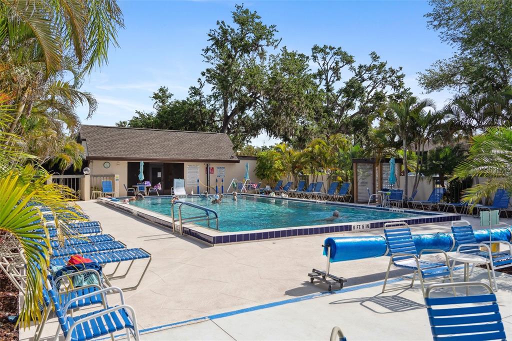 An outdoor swimming pool surrounded by lounge chairs and palm trees near a small building — 19505 QUESADA AVENUE UNIT J204, PORT CHARLOTTE, FL