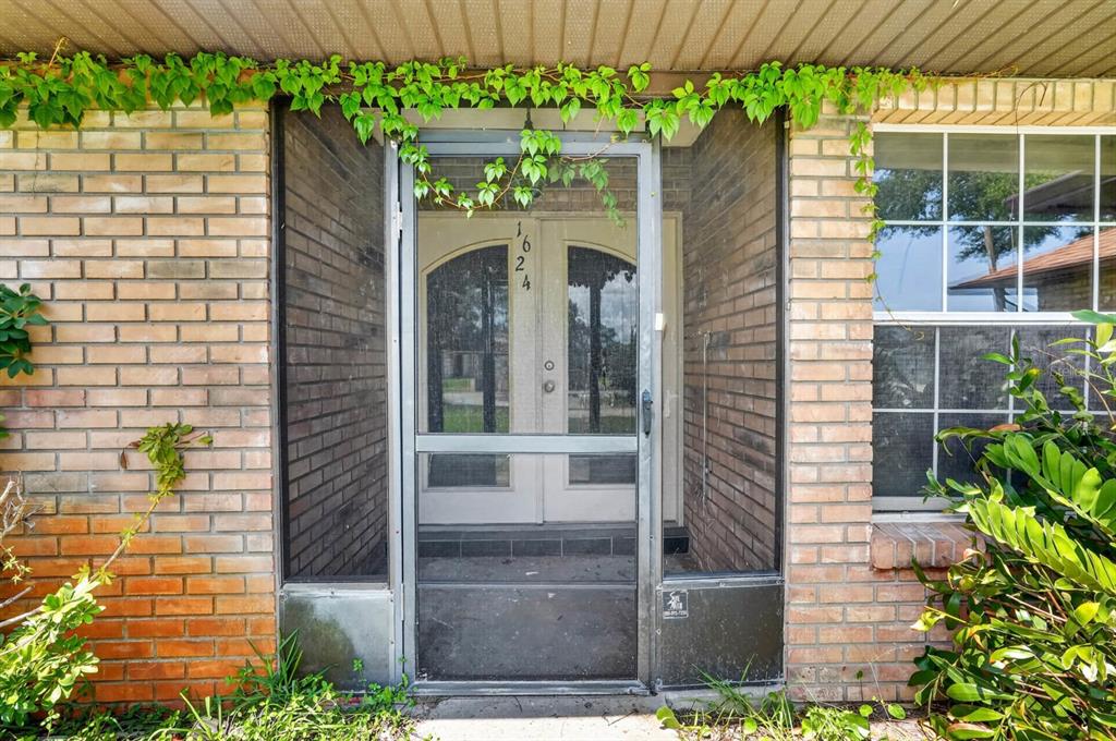 A brick house exterior features a screened front door with house numbers and climbing ivy — 1624 PICCADILLY DRIVE, DAYTONA BEACH, FL