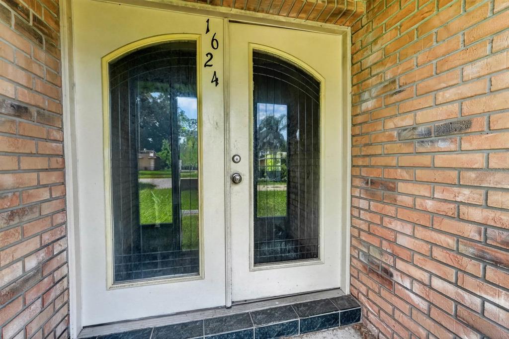 A double front door with arched glass panels is set into a brick exterior wall — 1624 PICCADILLY DRIVE, DAYTONA BEACH, FL