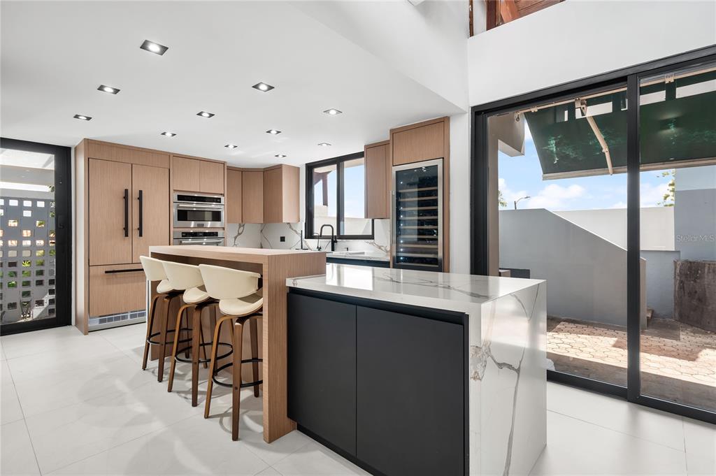 A modern kitchen features light wood cabinetry, a black island with marble countertops, and bar seating — 58 C, GUAYNABO, PR