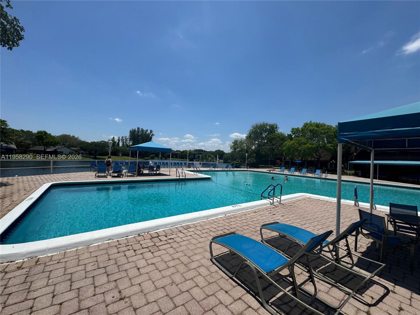An outdoor swimming pool with lounge chairs and blue shade structures on a brick deck — 3720 Inverrary Dr # 2S, Lauderhill FL 33319, LAUDERHILL, FL