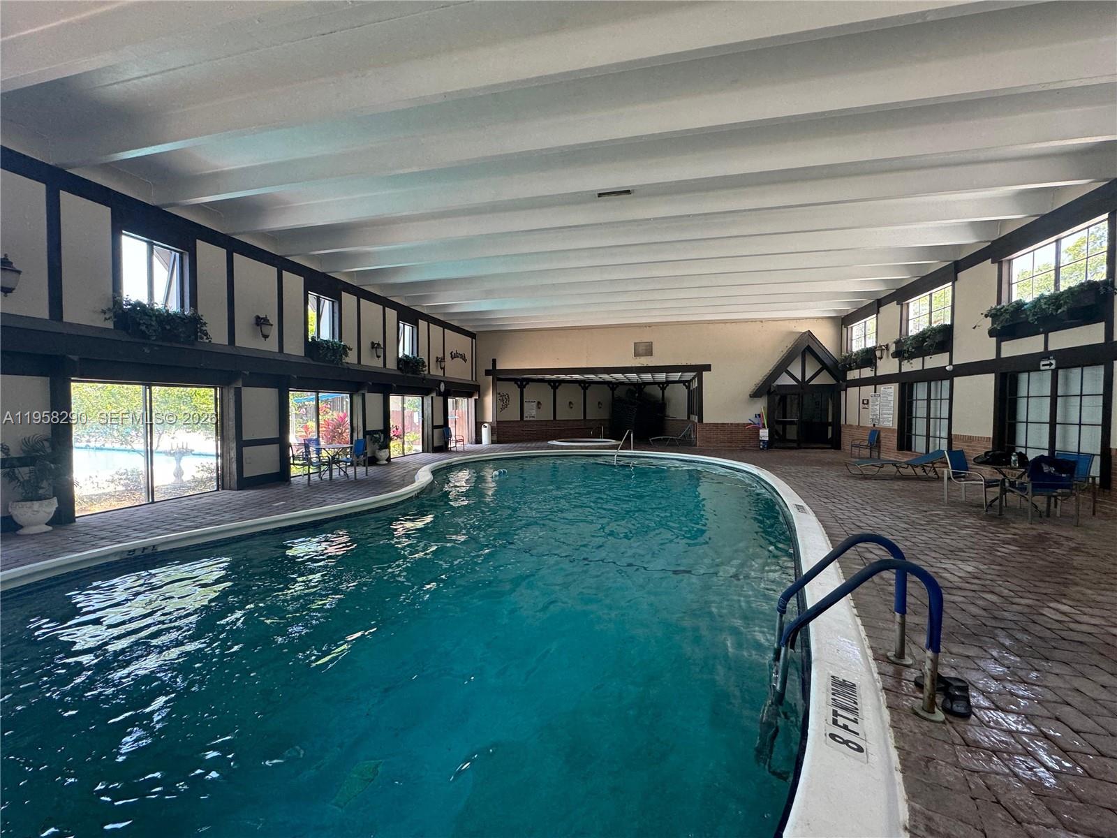 An indoor swimming pool area features a curved pool, brick flooring, and white beamed ceilings — 3720 Inverrary Dr # 2S, Lauderhill FL 33319, LAUDERHILL, FL