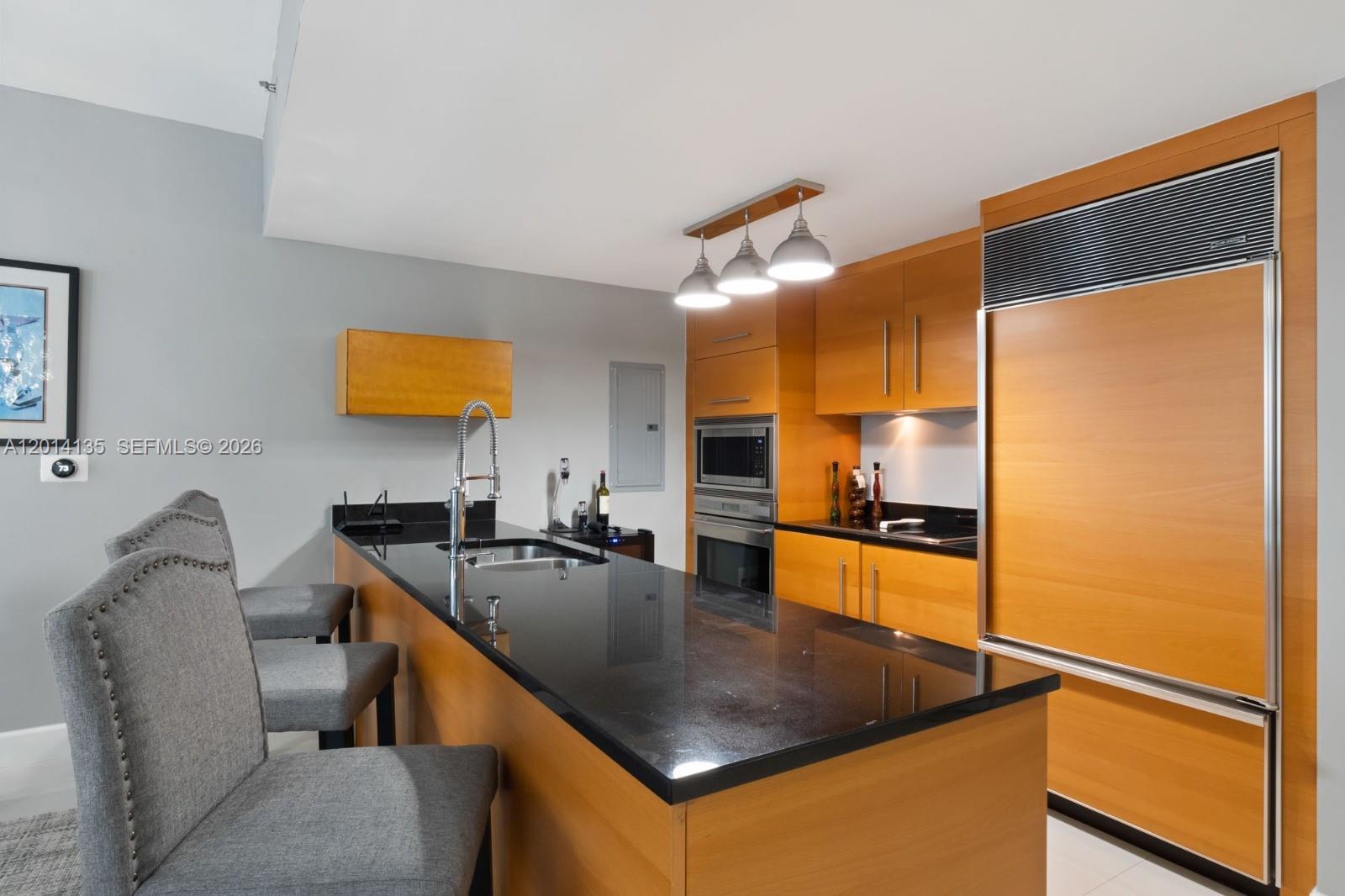 A modern kitchen features light wood cabinetry, black countertops, a breakfast bar, and stainless appliances — 475 Brickell Ave # 5109, Miami FL 33131, MIAMI, FL