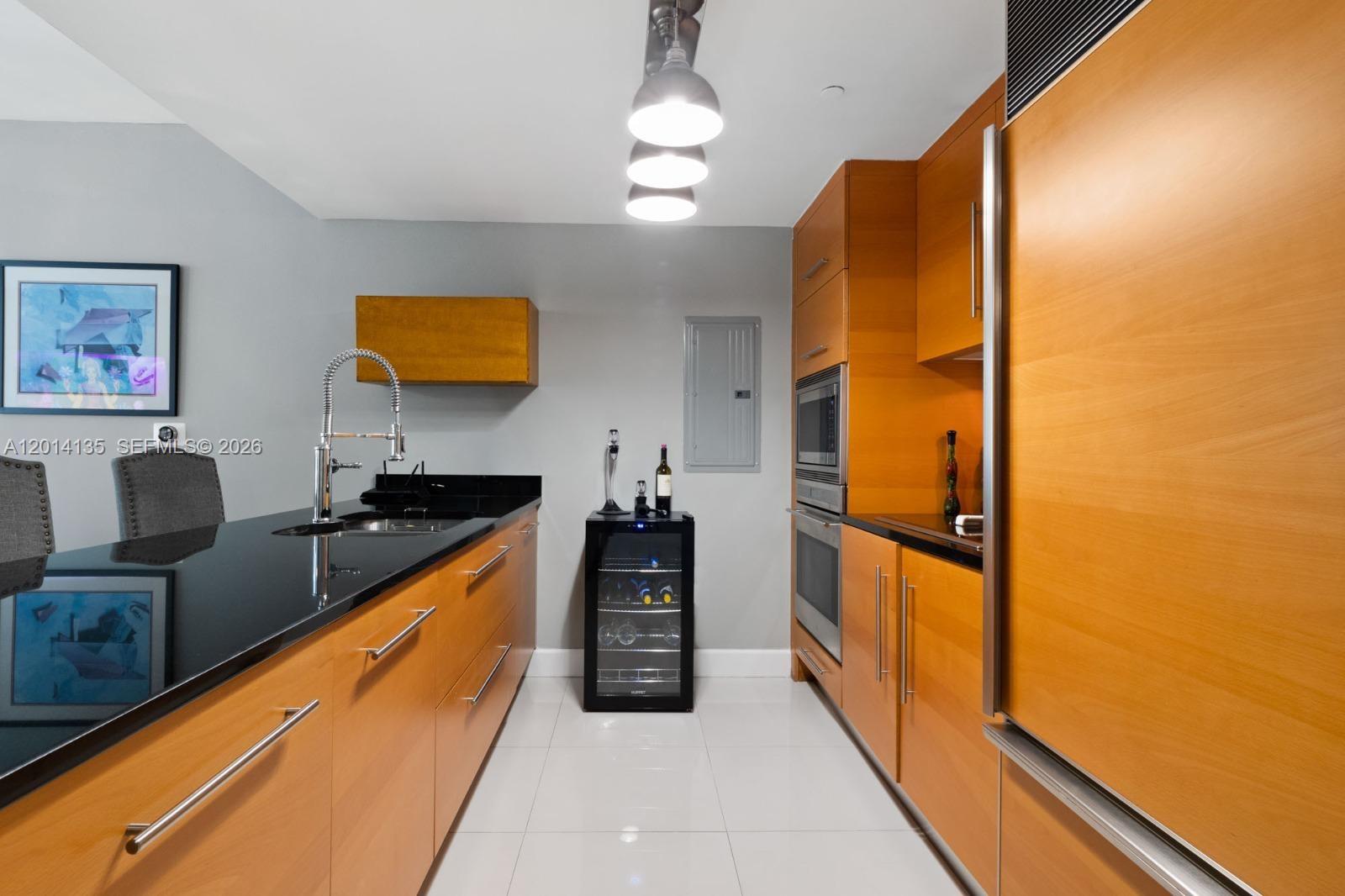 A modern kitchen features light wood cabinetry, black countertops, and stainless steel appliances — 475 Brickell Ave # 5109, Miami FL 33131, MIAMI, FL