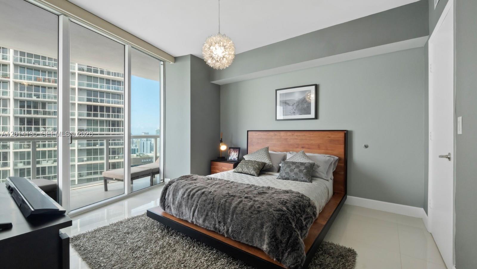 A bedroom with a platform bed, gray walls, and a balcony overlooking city buildings — 475 Brickell Ave # 5109, Miami FL 33131, MIAMI, FL