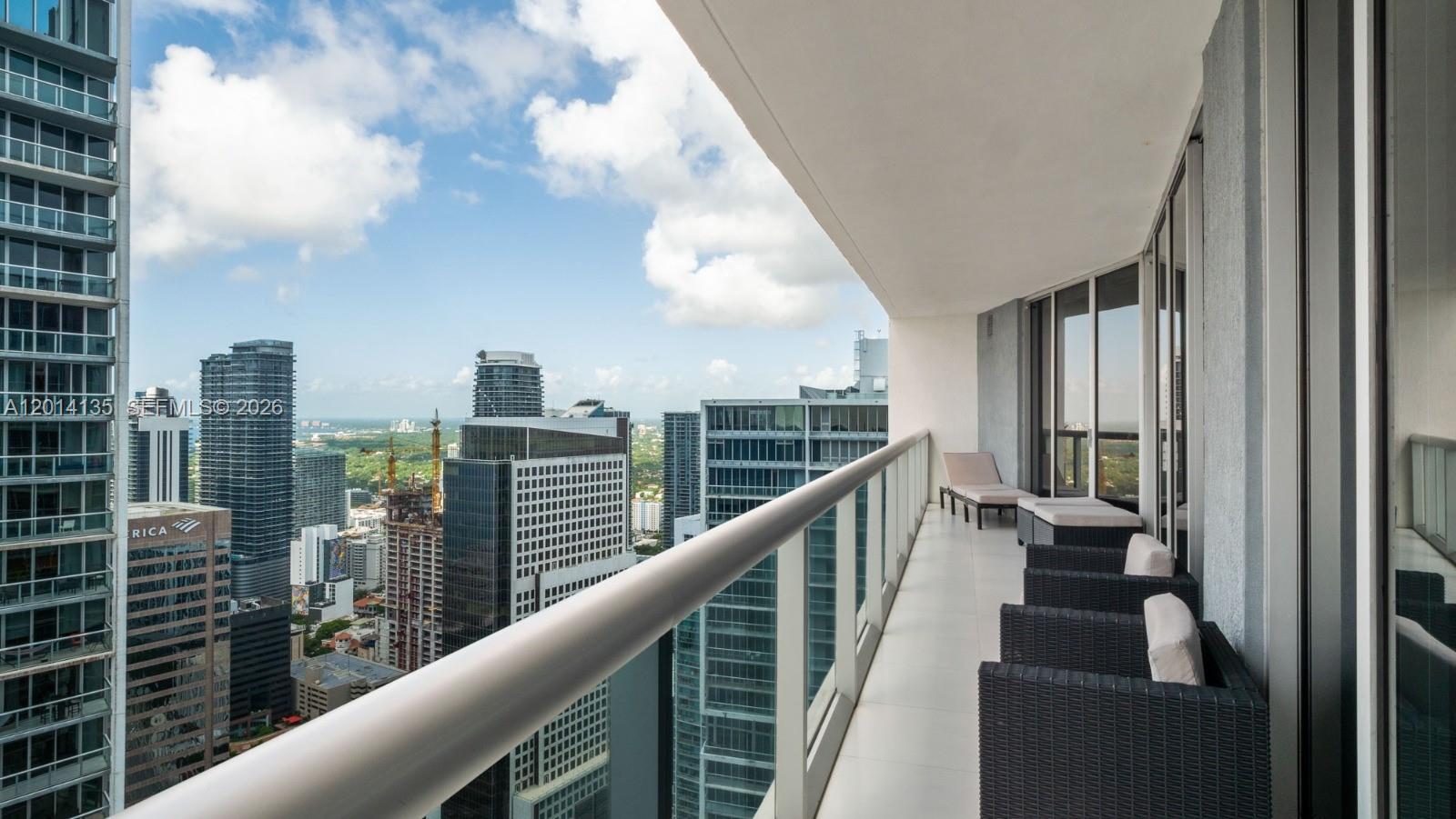 A high-rise balcony features outdoor furniture overlooking a dense urban skyline under a cloudy sky — 475 Brickell Ave # 5109, Miami FL 33131, MIAMI, FL