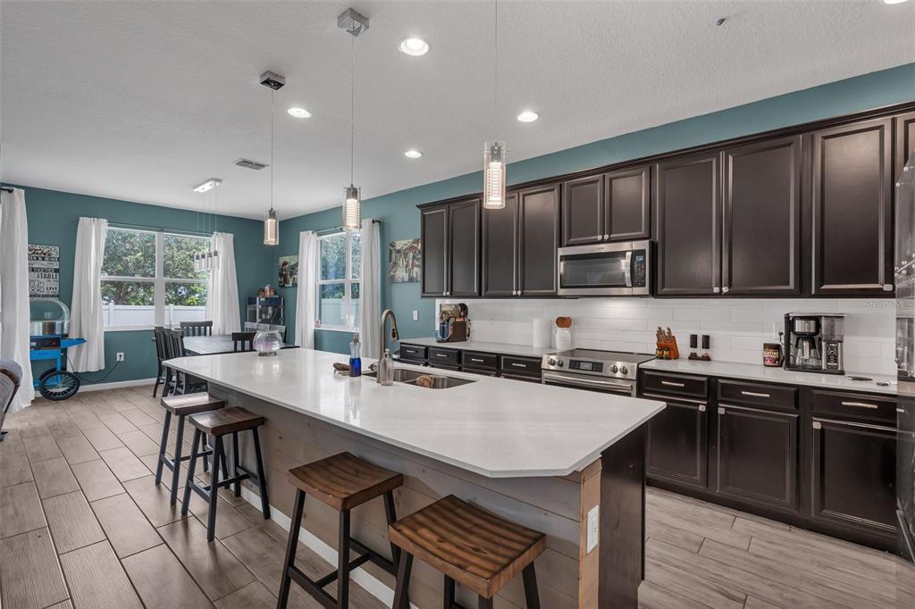 A kitchen features dark wood cabinets, a large white quartz island, and wood-look tile flooring — 822 OPAL COURT, DAVENPORT, FL