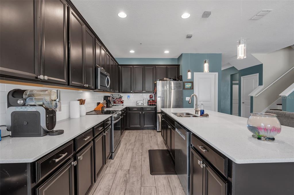 A kitchen features dark cabinetry, white countertops, stainless steel appliances, and wood-look tile flooring — 822 OPAL COURT, DAVENPORT, FL