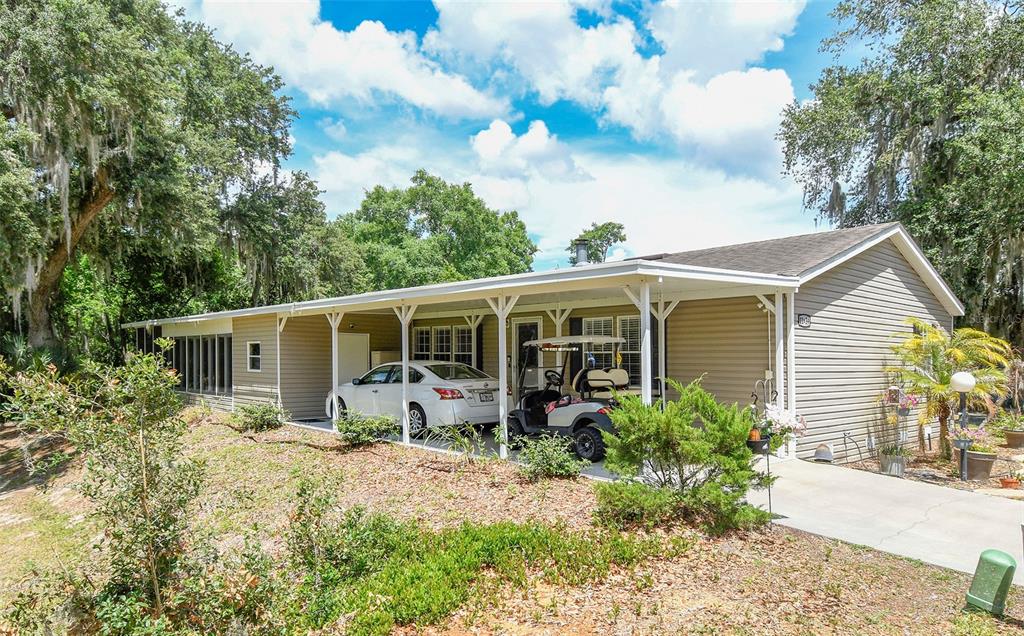 A single-story house with beige siding, a large carport, and a golf cart parked outside — 11639 MARTELL COURT, LEESBURG, FL