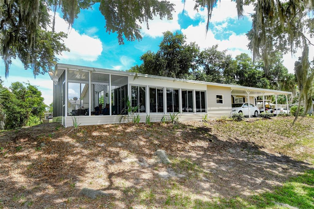 A single-story house with a large screened-in porch and an attached carport under oak trees — 11639 MARTELL COURT, LEESBURG, FL