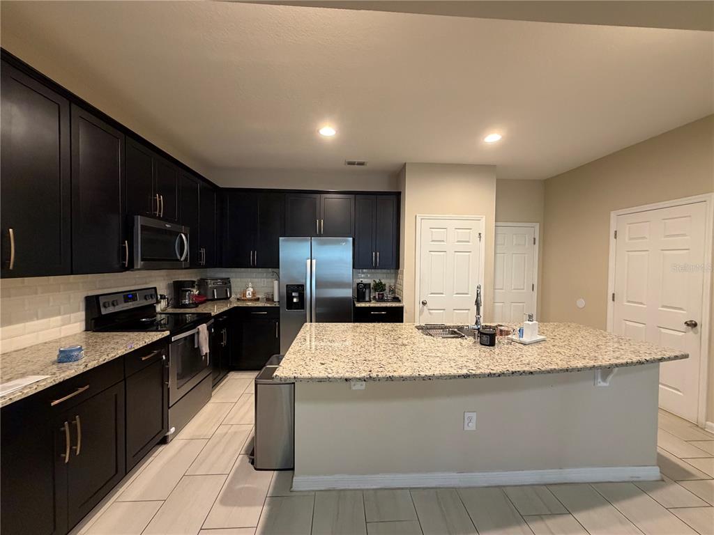 A kitchen features dark cabinetry, granite countertops, a central island, and light-colored tile flooring — 5686 CYPRESS HILL ROAD, WINTER GARDEN, FL