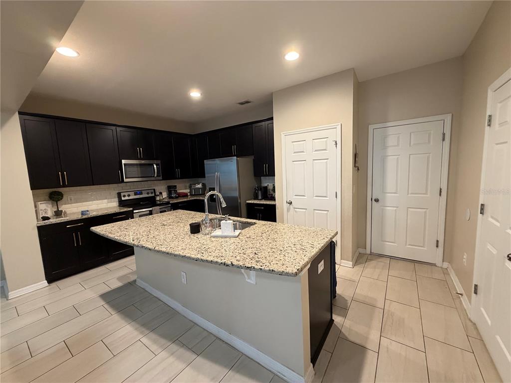 A kitchen features dark cabinets, granite countertops, a central island, and light-colored tile flooring — 5686 CYPRESS HILL ROAD, WINTER GARDEN, FL