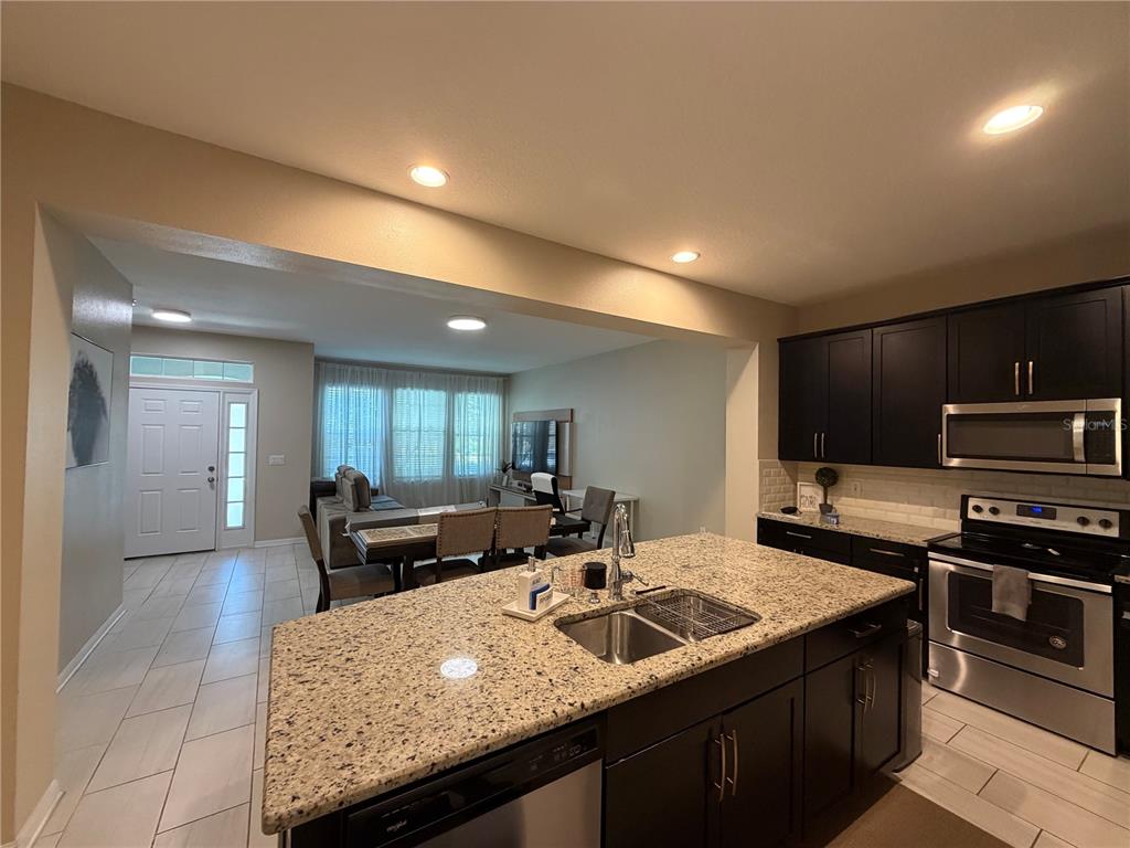 A kitchen with granite countertops and dark cabinets overlooks a living and dining area — 5686 CYPRESS HILL ROAD, WINTER GARDEN, FL