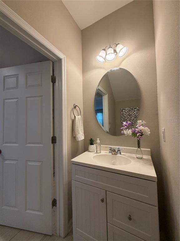 A bathroom features a white vanity, an oval mirror, and a three-light wall fixture — 5686 CYPRESS HILL ROAD, WINTER GARDEN, FL