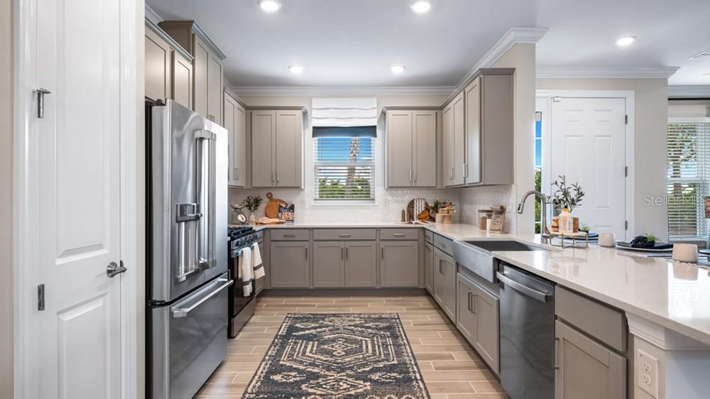 A modern kitchen features gray cabinets, stainless steel appliances, white countertops, and a patterned rug — 3867 FRACCARETA WAY, WESLEY CHAPEL, FL