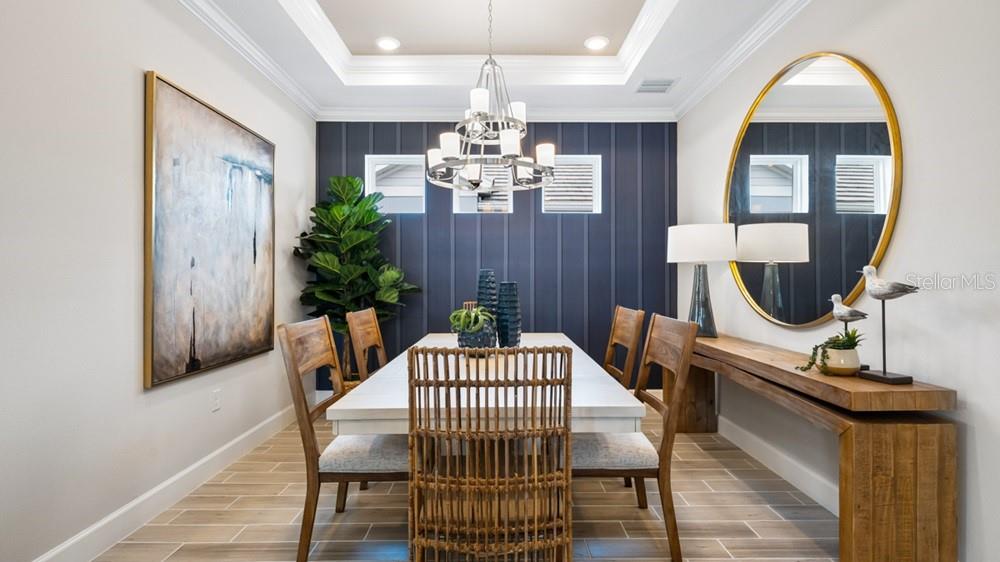 A dining room features a white table, wooden chairs, a dark blue accent wall, and chandelier — 3867 FRACCARETA WAY, WESLEY CHAPEL, FL
