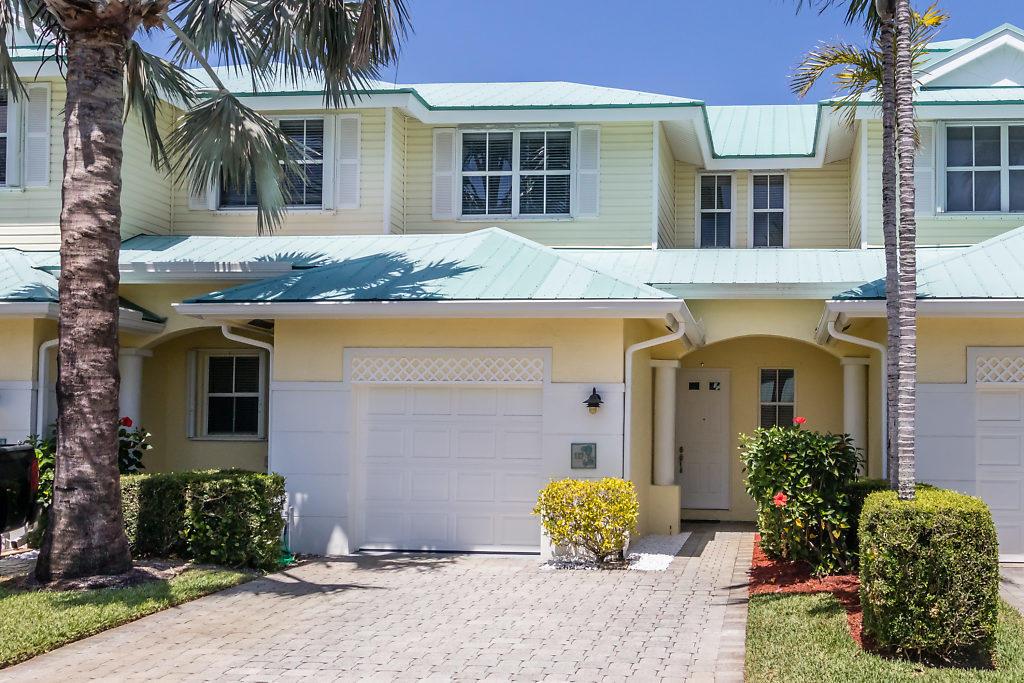 A two-story yellow townhouse with a teal metal roof, a garage, and a paved driveway — 117 Barefoot Cove, Hypoluxo FL 33462, HYPOLUXO, FL