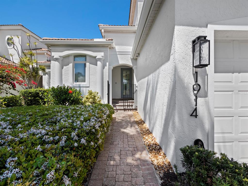 A paved walkway leads to a gated courtyard entrance of a white stucco house — 1914 HARBOUR LINKS CIRCLE UNIT 10, LONGBOAT KEY, FL