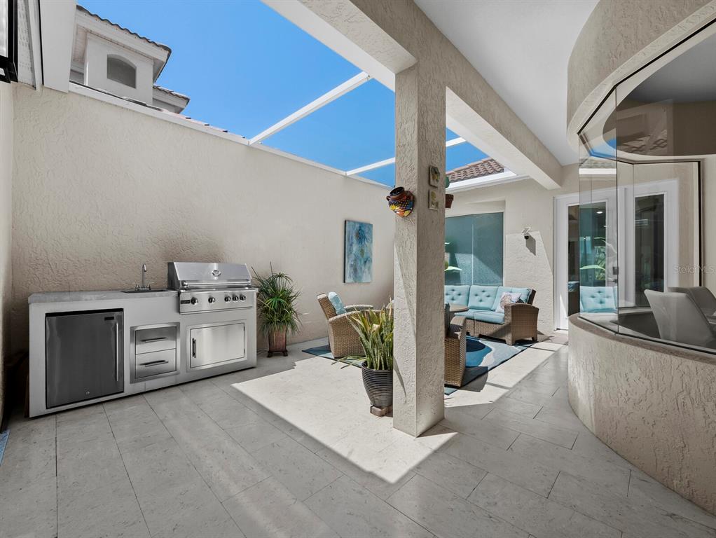 A covered outdoor patio features a stainless steel grill, a small refrigerator, and seating furniture — 1914 HARBOUR LINKS CIRCLE UNIT 10, LONGBOAT KEY, FL