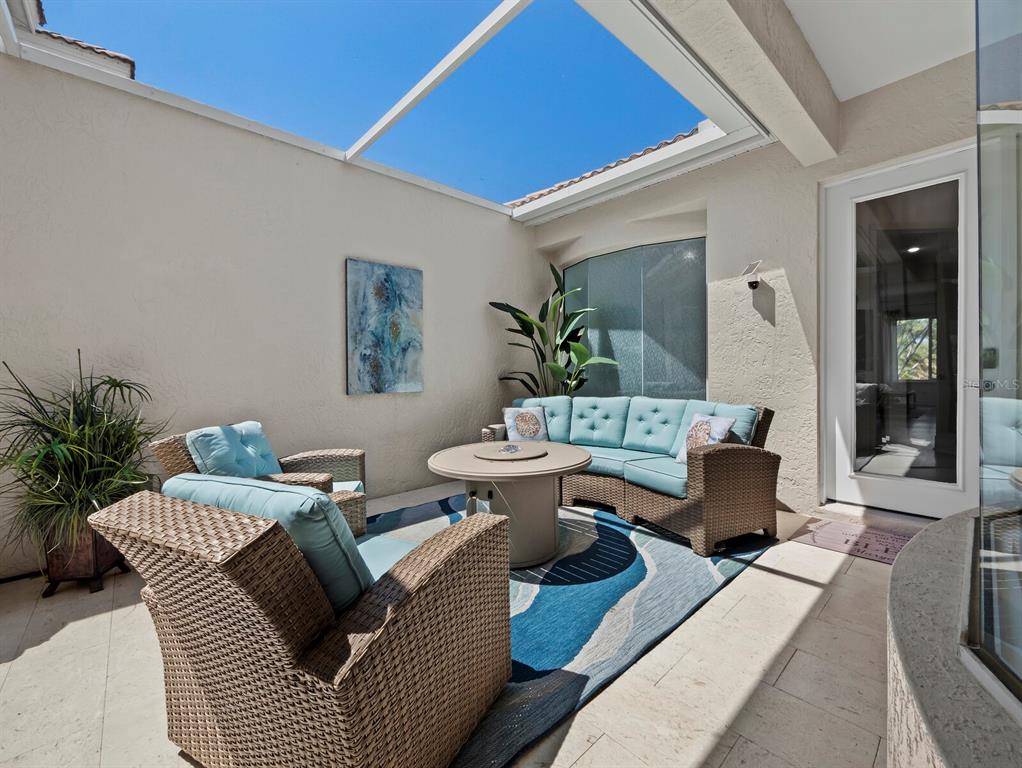 An outdoor patio features wicker furniture with blue cushions, a fire pit, and a skylight — 1914 HARBOUR LINKS CIRCLE UNIT 10, LONGBOAT KEY, FL