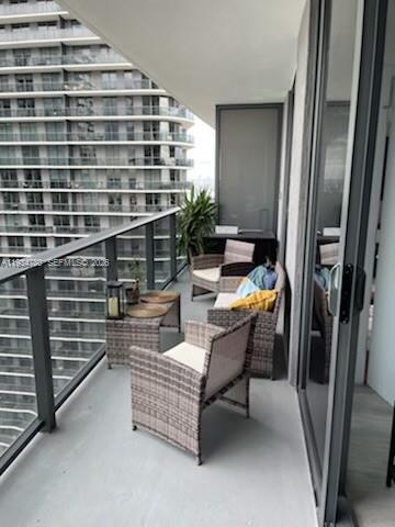 A balcony with wicker chairs and a small table overlooking a high-rise building — 45 SW 9th St # 3210, Miami FL 33130, MIAMI, FL