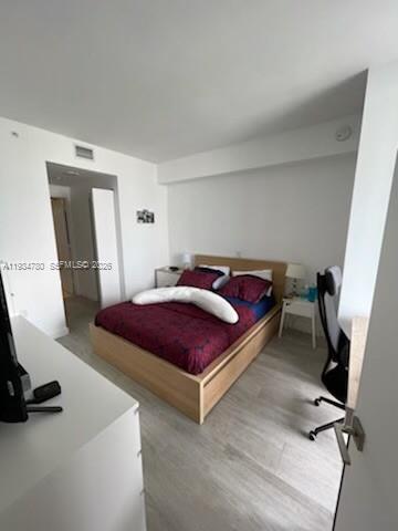 A bedroom features a wooden bed frame, light wood flooring, and a desk with a chair — 45 SW 9th St # 3210, Miami FL 33130, MIAMI, FL