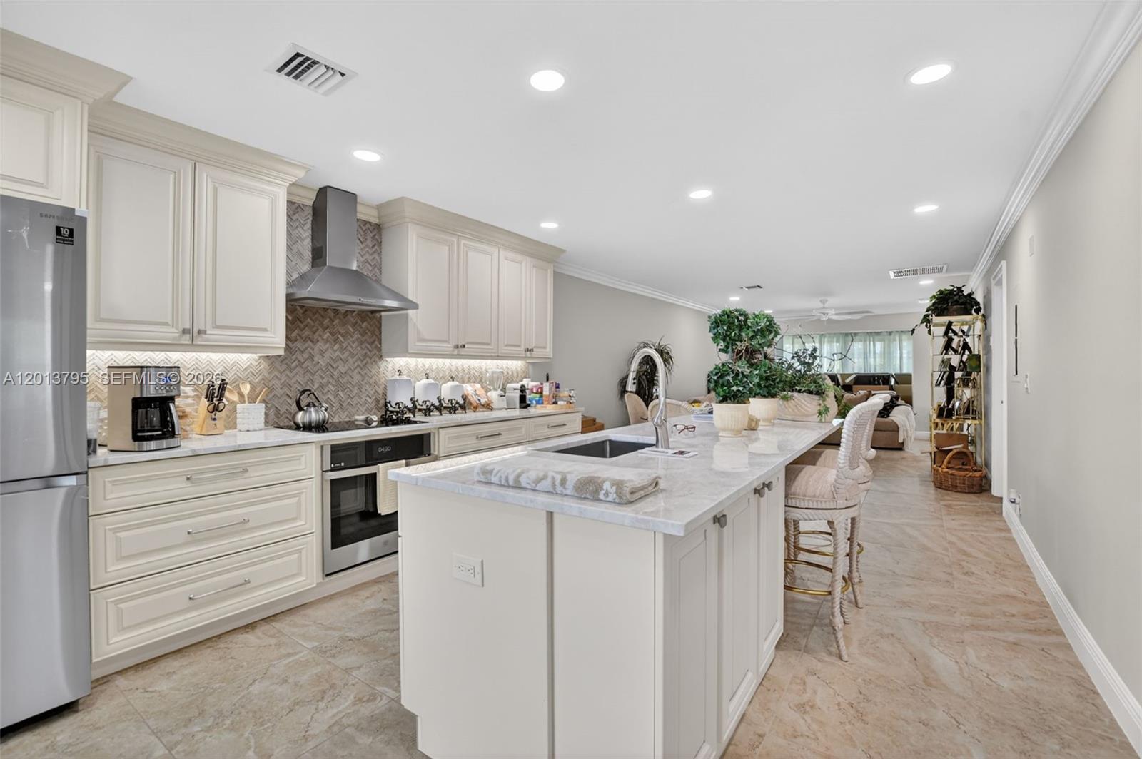 A modern kitchen features white cabinetry, a marble-topped island, and stainless steel appliances — 8749 Belle Aire Dr, Boca Raton FL 33433, BOCA RATON, FL