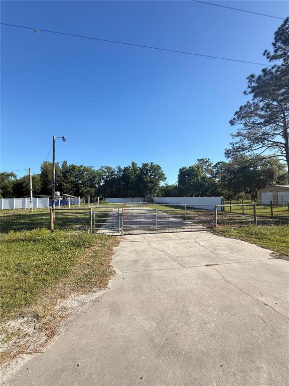 A concrete driveway leads to a metal gate and fenced property with trees in the background — 19651 CAUSEWAY BOULEVARD, LAND O LAKES, FL