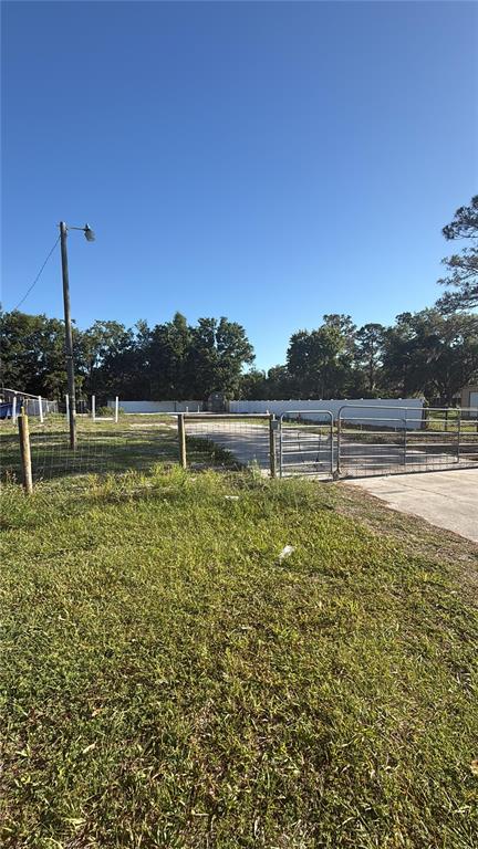 A fenced, grassy lot features a metal gate and a utility pole under a clear sky — 19651 CAUSEWAY BOULEVARD, LAND O LAKES, FL