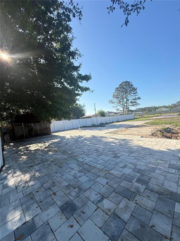 A large backyard features a paved patio, a white vinyl fence, and mature trees — 19651 CAUSEWAY BOULEVARD, LAND O LAKES, FL