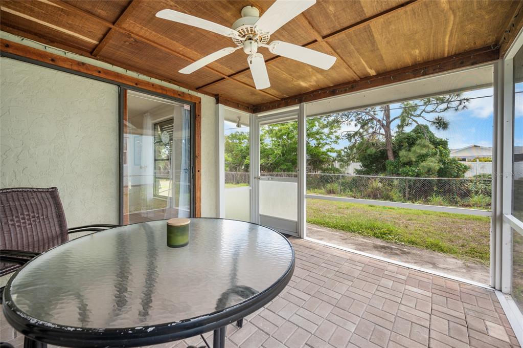 A screened-in patio with a wood-paneled ceiling, ceiling fan, glass table, and paver flooring — 901 PONDEROSA ROAD, VENICE, FL