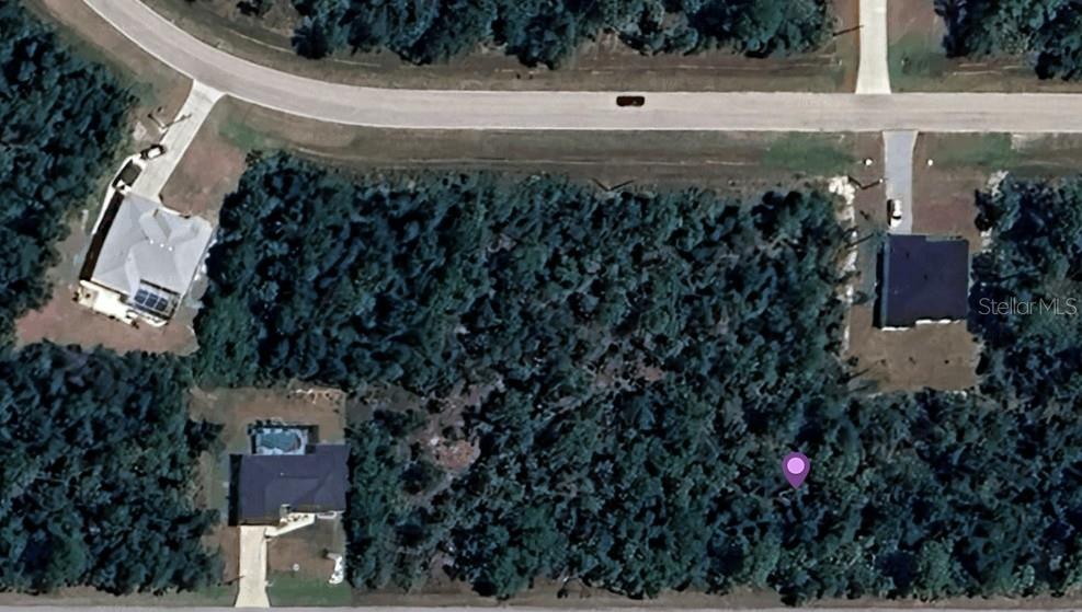 This aerial view shows a wooded vacant lot situated between three existing residential properties — 14378 CAROUSEL LANE, PORT CHARLOTTE, FL