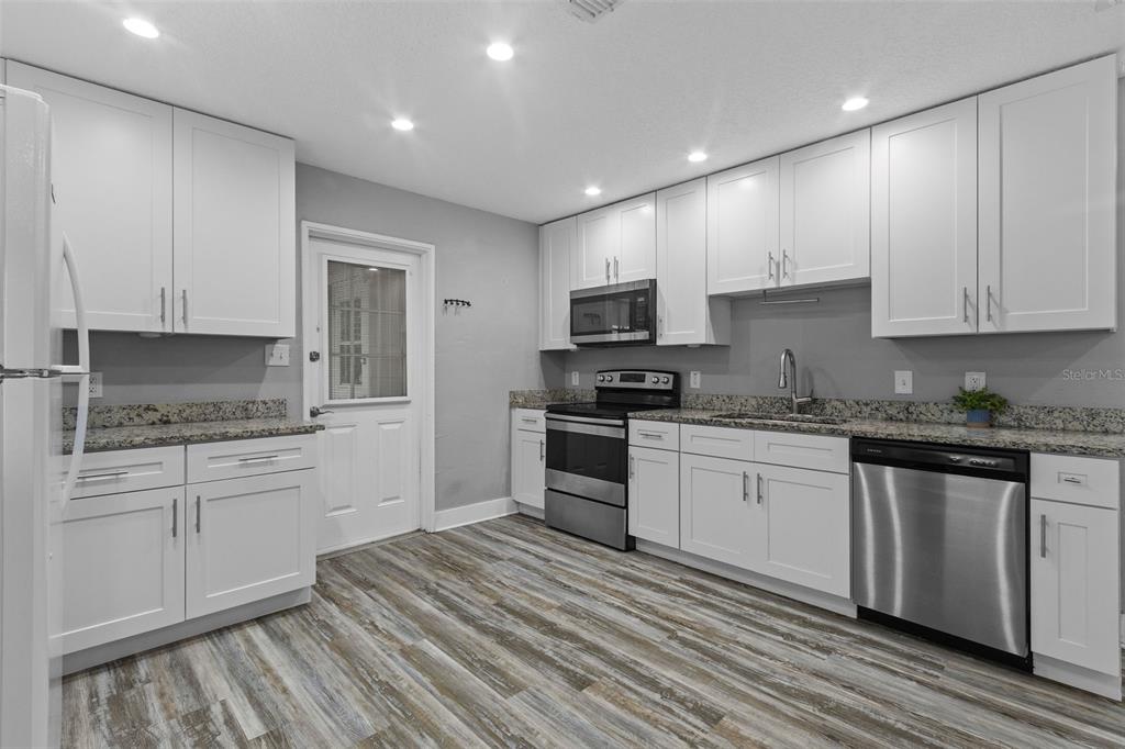 A kitchen with white cabinets, granite countertops, stainless steel appliances, and wood-look flooring — 4402 W TRILBY AVENUE, TAMPA, FL