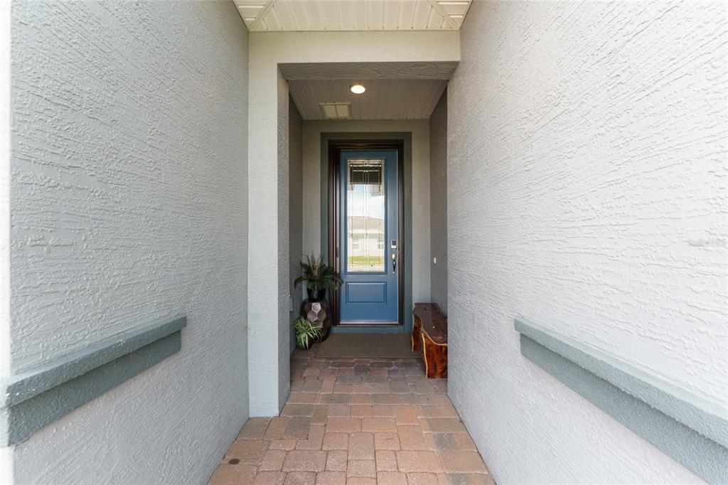 A covered entryway features a blue front door, stone paver flooring, and stucco walls — 5613 NW 40TH LOOP, OCALA, FL