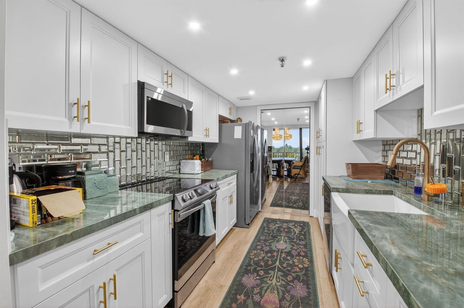 A galley kitchen features white cabinets, green stone countertops, gold hardware, and a mirrored backsplash — 899 Jeffery Street # 5100, Boca Raton FL 33487, BOCA RATON, FL