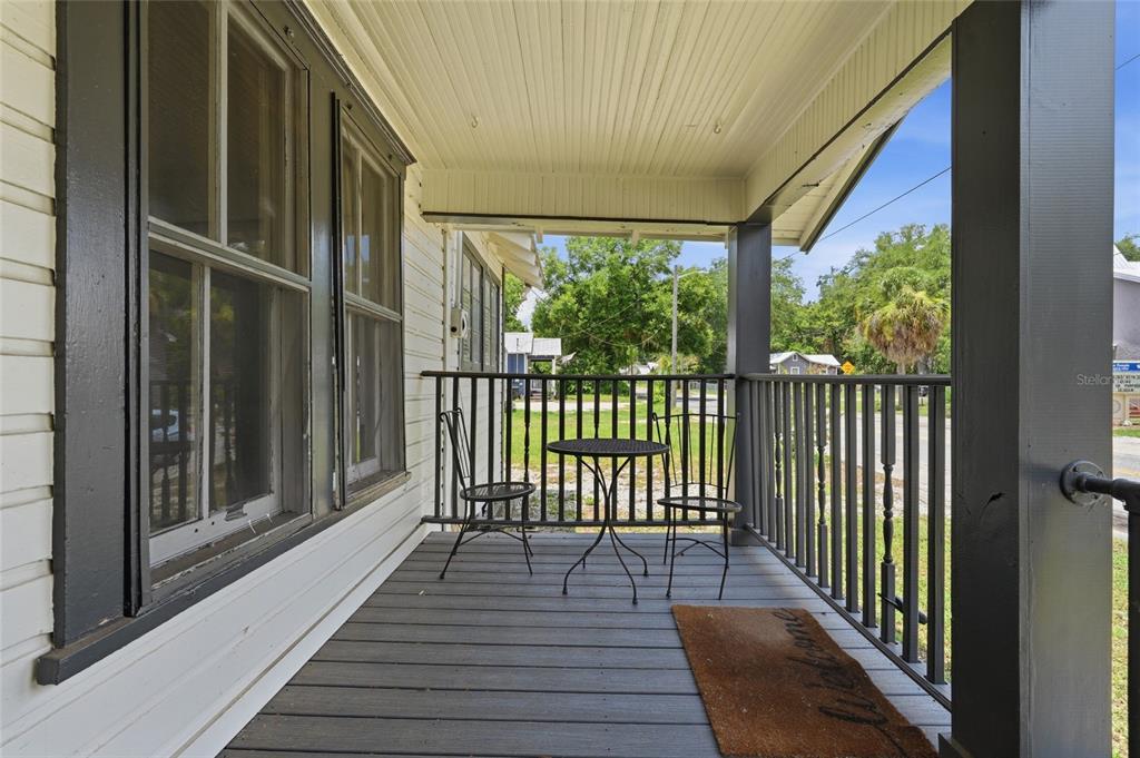 A covered porch features dark wooden decking, a small bistro set, and a welcome mat — 619 NW 7TH AVENUE, GAINESVILLE, FL