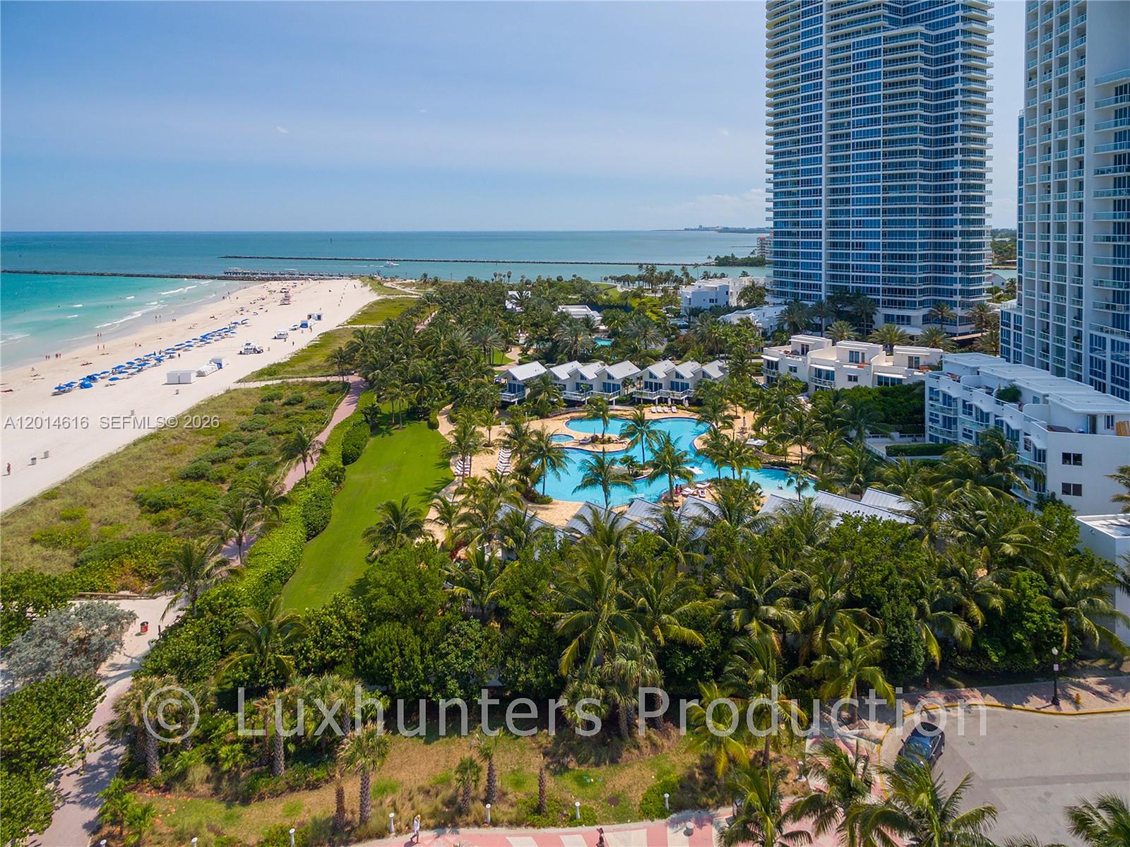 An aerial view shows a beach, a swimming pool, palm trees, and high-rise buildings — 50 S Pointe Dr # 607, Miami Beach FL 33139, MIAMI BEACH, FL