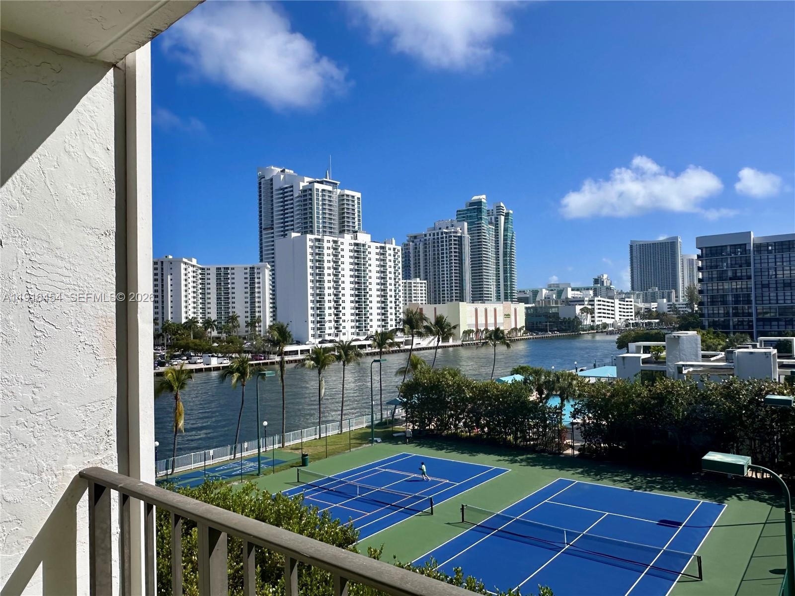 A balcony view overlooks two blue tennis courts, a waterway, and high-rise buildings — 1000 Parkview Dr # 518, Hallandale Beach FL 33009, HALLANDALE BEACH, FL