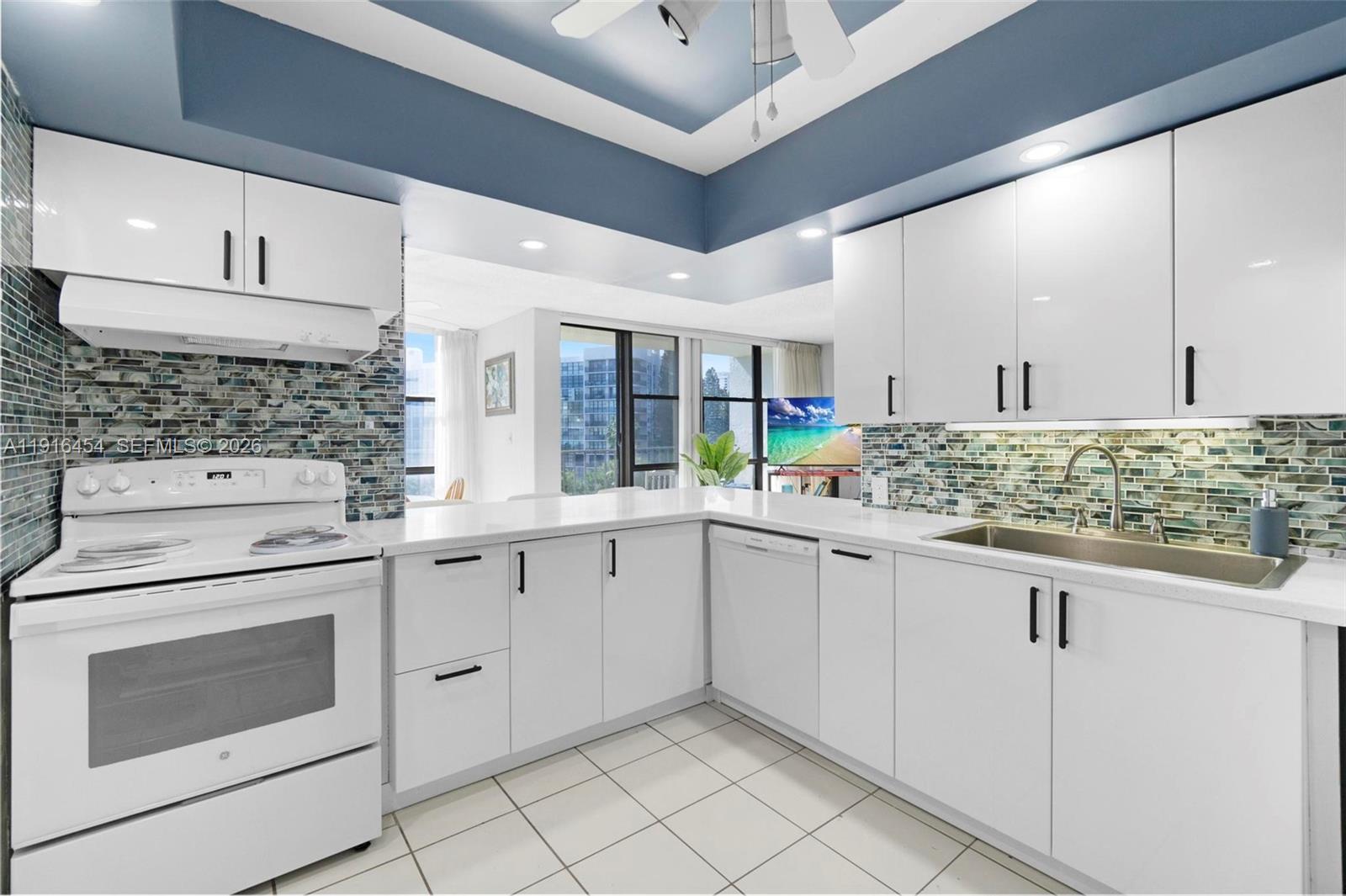 A kitchen features white cabinets, a glass tile backsplash, and white countertops — 1000 Parkview Dr # 518, Hallandale Beach FL 33009, HALLANDALE BEACH, FL