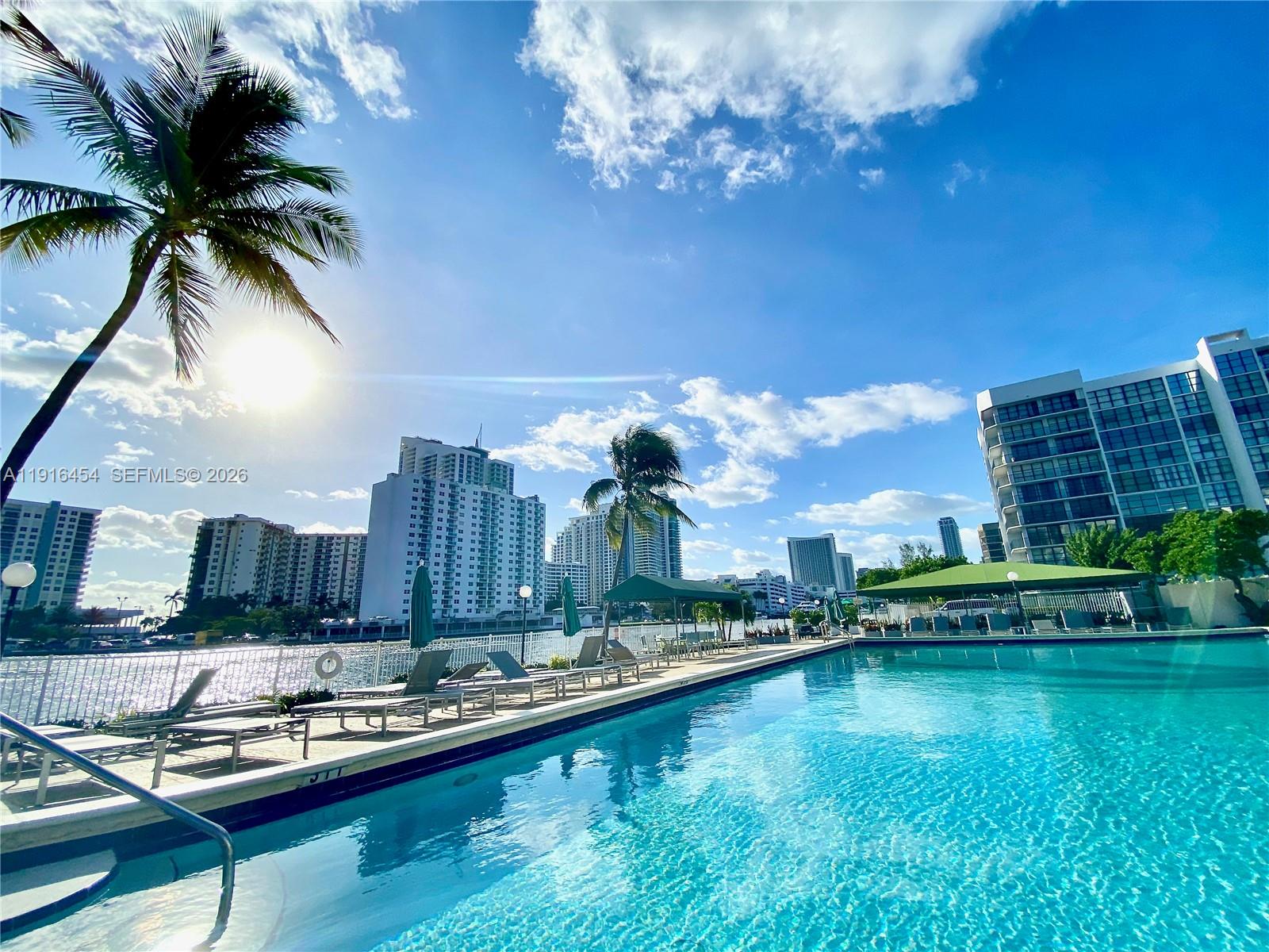 A swimming pool sits on a deck lined with lounge chairs and palm trees — 1000 Parkview Dr # 518, Hallandale Beach FL 33009, HALLANDALE BEACH, FL