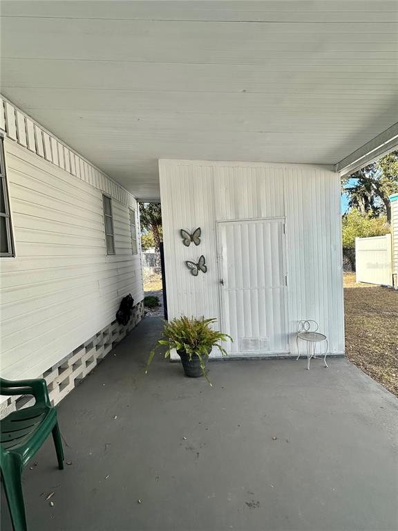 A covered concrete patio features a white door, two butterfly wall decorations, and a potted plant — 5619 BAYSHORE ROAD UNIT 328, PALMETTO, FL