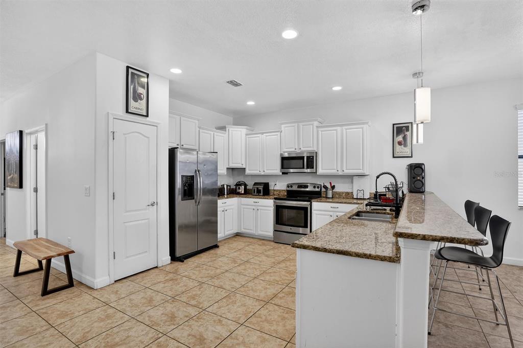 A kitchen with white cabinets, granite countertops, stainless steel appliances, and a breakfast bar — 9107 EL CARO LANE, DAVENPORT, FL