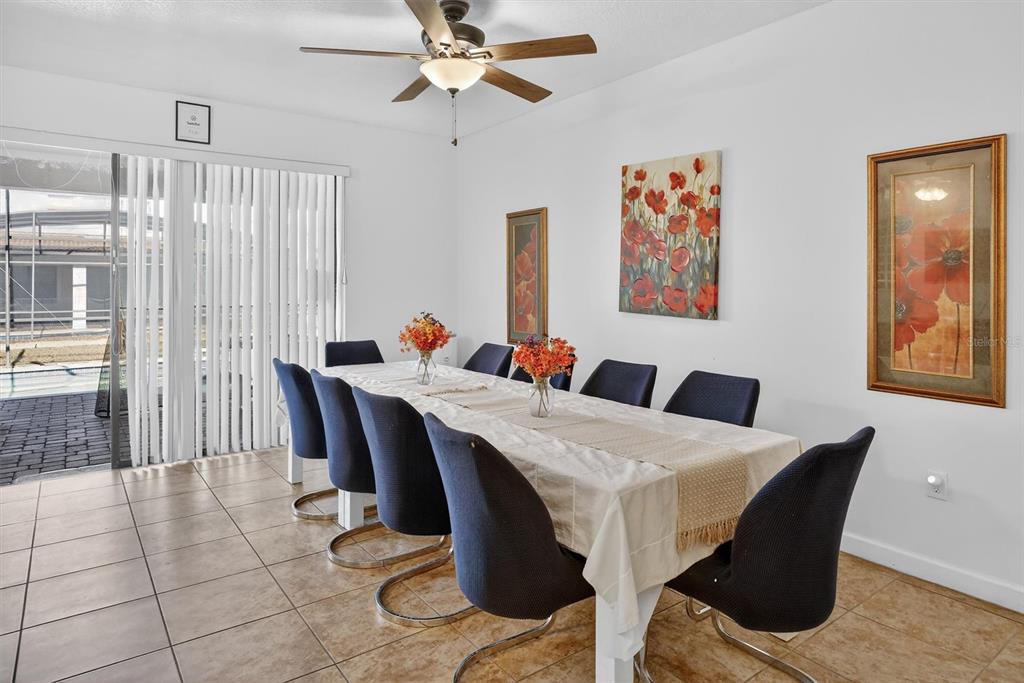 A dining room features a long table with blue chairs, tile floors, and wall art — 9107 EL CARO LANE, DAVENPORT, FL