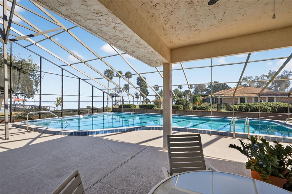 A screened-in pool patio overlooks a lake with outdoor furniture on a concrete deck — 301 CLUSTERWOOD DRIVE, YALAHA, FL