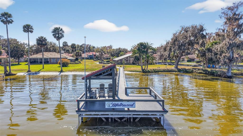 A wooden dock with a covered seating area extends into a lake near residential homes — 301 CLUSTERWOOD DRIVE, YALAHA, FL